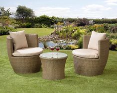 three wicker chairs and a table with a glass of wine on it in the grass