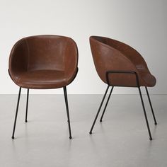 two brown chairs sitting next to each other on top of a cement floor in front of a white wall