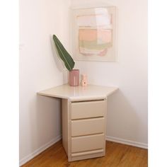 a small white table with a plant on top and a painting hanging above the table