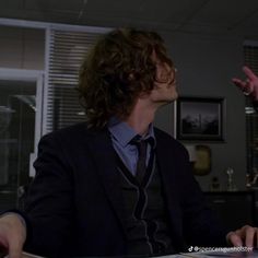 a man in a suit and tie sitting at a desk with his hand out to someone