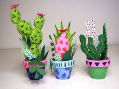 three potted plants are sitting on a white surface and one is made out of paper