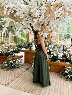 a woman in a green dress standing under a tree with white flowers and greenery