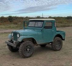 an old green truck is parked in the dirt