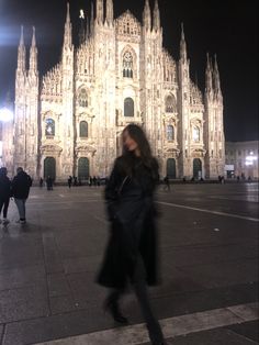 a woman walking in front of a large cathedral at night