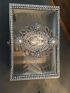 an ornate silver frame with pearls and jewels on it is hanging from the wall in front of a window