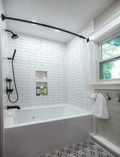 a white tiled bathroom with black fixtures and tile flooring on the walls, along with a large bathtub