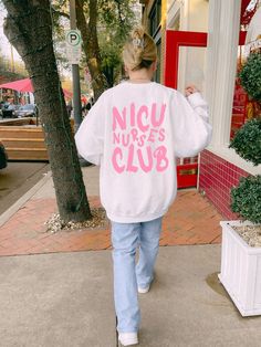 a woman walking down the street wearing a sweater that says nicu nurse's club