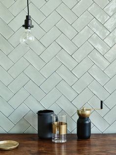 three vases on a wooden table in front of a white wall with herringbone tiles