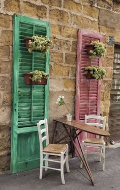 two chairs and a table in front of an old brick building with shuttered windows