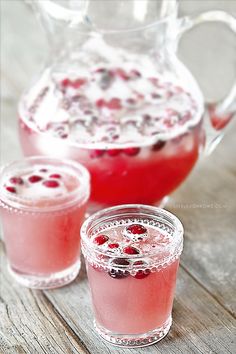 two glasses filled with liquid and garnished with cranberries next to a pitcher