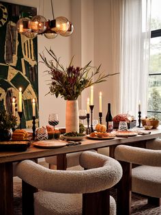 a dining room table set with candles, plates and bowls on it's centerpiece