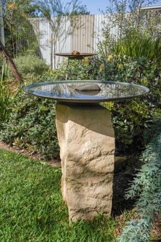 a stone table with a glass top in the middle of some grass and plants around it