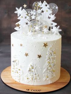 a white frosted cake with gold stars and snowflakes on the top is sitting on a wooden platter