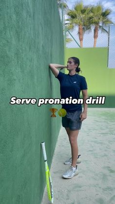 a woman leaning against a green wall with a tennis racket and ball in her hand