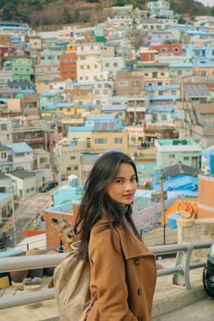 a woman standing in front of a city with lots of buildings on the hill behind her