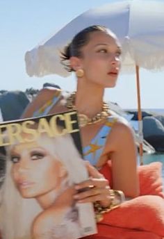 a woman sitting on the beach holding a magazine