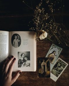 an open book sitting on top of a wooden table next to flowers and pictures in front of it