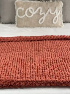 an orange blanket on top of a bed next to a pillow with the word cozy written across it