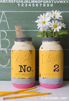 two jars with flowers in them sitting on a table next to pencils and a chalkboard