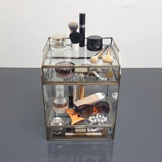 an assortment of cosmetics and makeup products in a glass container on a table with white walls