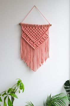 a pink wall hanging on the side of a white wall next to a potted plant