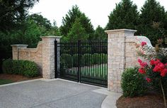 a gated driveway with flowers and bushes around it