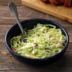 a blue bowl filled with coleslaw on top of a wooden table next to a cutting board