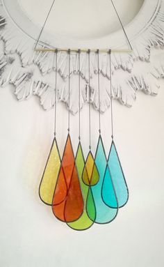 a wind chime hanging from the side of a wall with four different colored drops on it