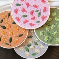 four different colored embroidery designs on small hoops with green leaves and orange slices in the center