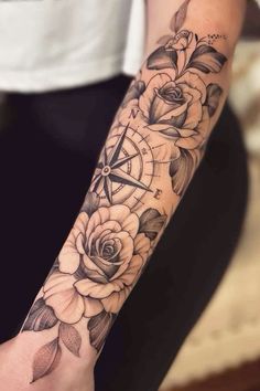 a woman's arm with roses and compass tattoo on it