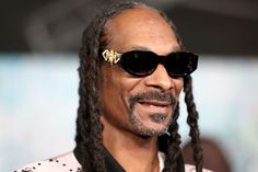 a close up of a person wearing sunglasses and dreadlocks with a smile on his face