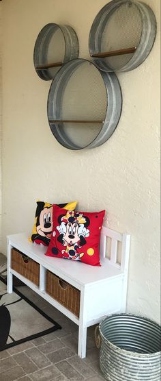 a white bench with mickey mouse pillows on it next to two round metal wall hangings