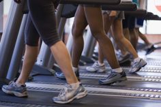 several people are running on treadmills in a gym or exercise room, with their feet resting on each other's legs