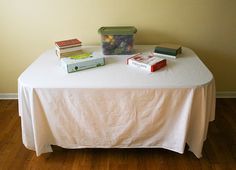 a table topped with books on top of a white table cloth covered table next to a yellow wall