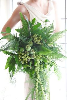 a woman in a white dress holding a large bouquet of green plants and foliages