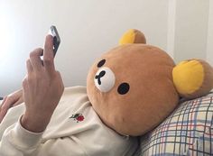 a person holding a cell phone up to their face while laying in bed with a stuffed animal