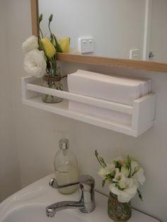 a bathroom sink with flowers and soap on the shelf next to it in front of a mirror