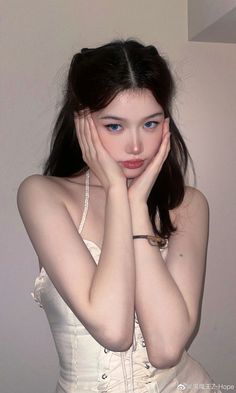 a woman in a white dress posing for the camera with her hands on her face