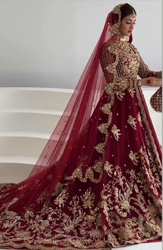 a woman in a red and gold bridal gown standing next to a white wall