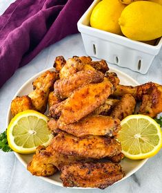 chicken wings with lemons and parsley on a plate next to a basket of lemons