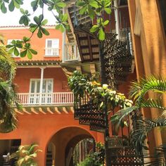 an orange building with lots of green plants in the courtyard and stairs leading up to it