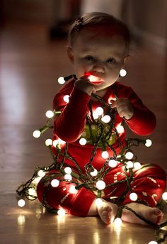 a baby sitting on the floor next to a christmas tree with lights all over it