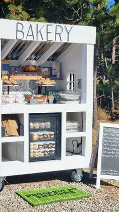 an outdoor bakery with lots of food on display in front of the counter and sign