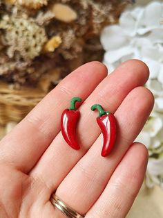 pair of red chili pepper shaped earrings with green leaves on top, in front of white flowers