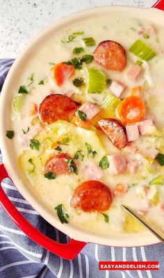 a bowl of soup with sausage, tomatoes and green onions in it next to a blue towel