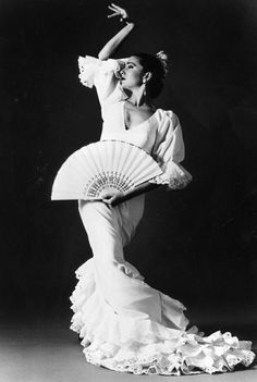 an old photo of a woman in a white dress holding a fan and posing for the camera