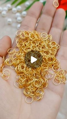 a person is holding some gold rings in their hand and there are red flowers behind them