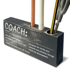 a wooden holder with pens and pencils in it that has the words coach written on it