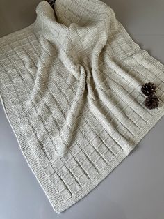 a white knitted blanket sitting on top of a table next to a pine cone