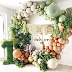 the balloon arch is decorated with balloons and greenery for an animal themed birthday party